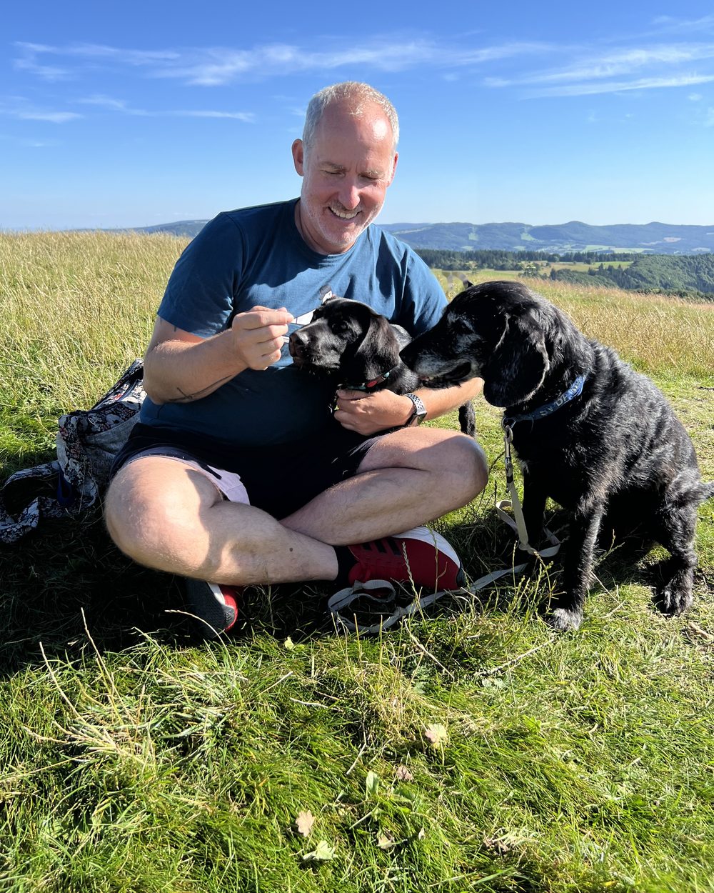 Janko Dreyer sitzt auf einer Wiese bei seinen beiden Hunden Joschi und Paula.